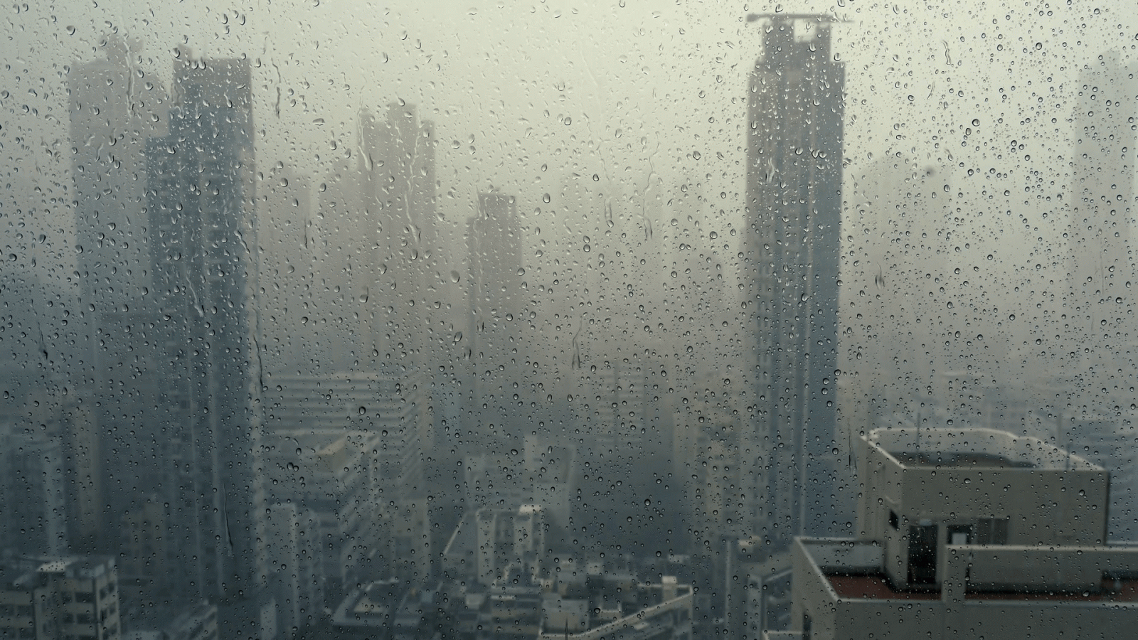1920x1080 Rain falling on window in skyscraper apartment. Dark and stormy rainy day  in big city life. View of dreary Hong Kong cityscape whilst rain drops fall 