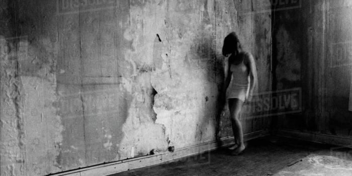 1200x840 Young woman walks alongside a battered old wall with wallpaper being ripped  off it wearing a short white dress stock photo